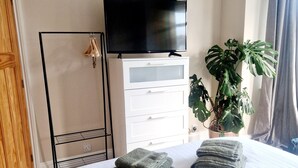 Une chambre d’hôtel avec un lit, un téléviseur posé sur une commode, une plante et une étagère avec des serviettes.