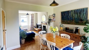 Un coin repas avec une table en bois et des chaises blanches, un grand tableau au mur et une vue sur le salon.