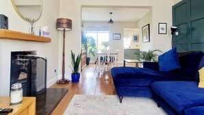 Un salon avec un canapé bleu, une cheminée, un coin repas avec une table et des chaises, et une cuisine à l’arrière-plan.