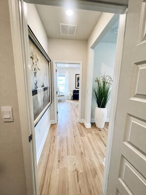 A hallway with wooden flooring, white walls, and a door leading to another room.