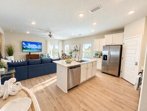 A modern kitchen with a stainless steel refrigerator, a dining area with a white table and blue sofa, and a ceiling fan.