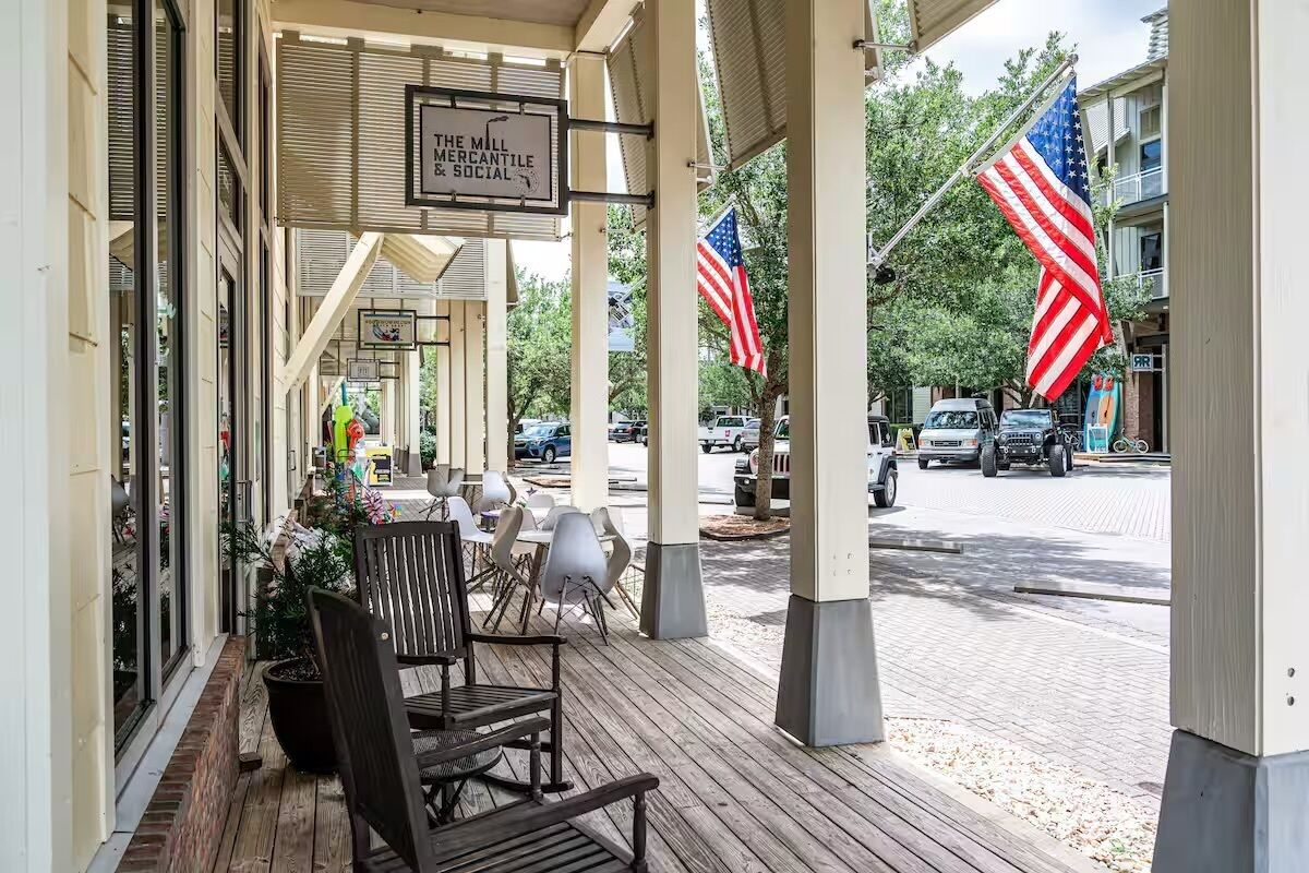 Ein überdachter Außenbereich mit Tischen und Stühlen, eine amerikanische Flagge und ein Schild mit der Aufschrift 'The Mill Mercantile & Social'.