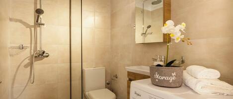 A modern bathroom with a glass-enclosed shower, a toilet, a sink with a mirror, and a washing machine.