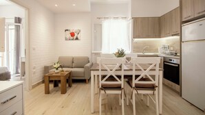Una cocina moderna con armarios blancos, un comedor con mesa y sillas blancas, y una mesita auxiliar con un florero y velas.