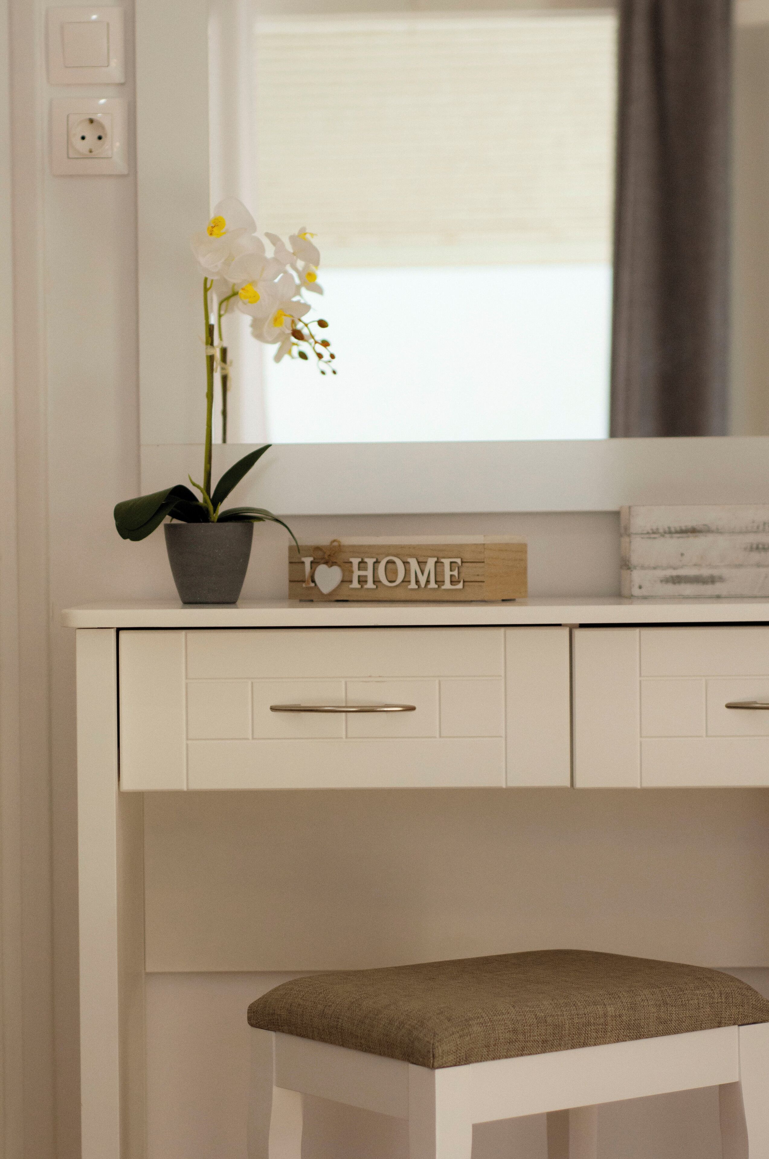 A white desk with a potted orchid, a 'I ♥ HOME' sign, and a bench.