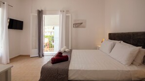 Habitación de hotel con cama, televisor de pantalla plana, balcón con vistas y puerta con cortinas.