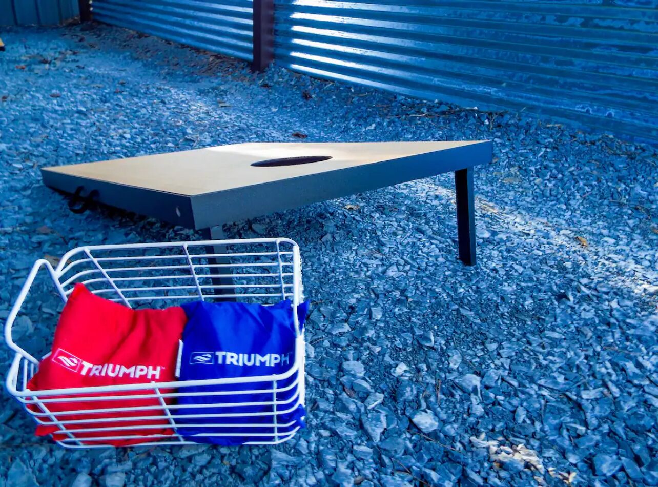 Un banc en métal avec un coussin et un panier à provisions contenant des sacs étiquetés « TRIUMPH », le tout posé sur un sol de gravier.