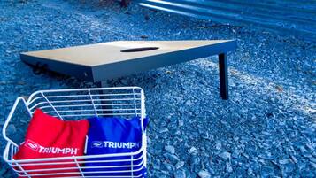 Un banc en métal avec un coussin et un panier à provisions contenant des sacs étiquetés « TRIUMPH », le tout posé sur un sol de gravier.