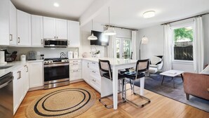 A modern kitchen with white cabinets, a stove, and a dining area with chairs and a table. - Montrose Manor- In the heart of Belmont! (Charlottesville)