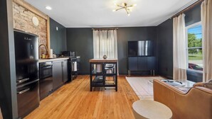 A modern kitchen with a brick wall, black appliances, and a dining area with a table and chairs. - Montrose Manor- In the heart of Belmont! (Charlottesville)