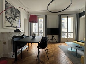 Uma sala de estar moderna com uma grande mesa de jantar, cadeiras pretas, lareira, TV fixada na parede e vista da cidade através de janelas amplas.