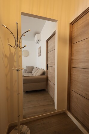 Un couloir avec un plancher en bois, un porte-manteau, un canapé avec des coussins, un miroir et une porte en bois.