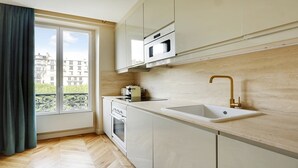 A modern kitchen with white cabinets, a built-in oven, a microwave, and a sink with a gold faucet.
