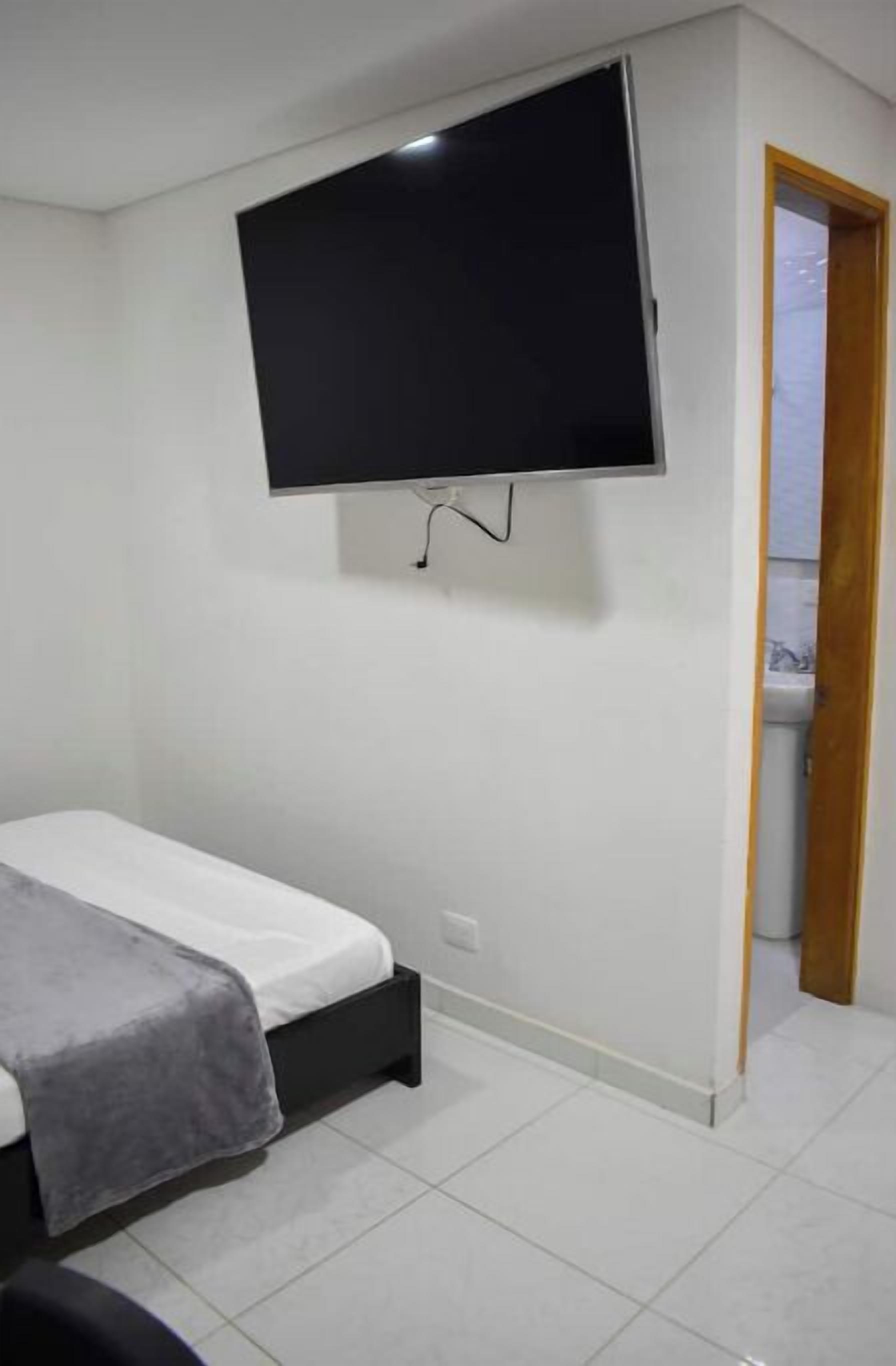 A bedroom with a bed, a flat-screen TV mounted on the wall, and a door leading to a bathroom.