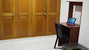 A bedroom with a bed, a desk with a laptop, a chair, and a wardrobe.