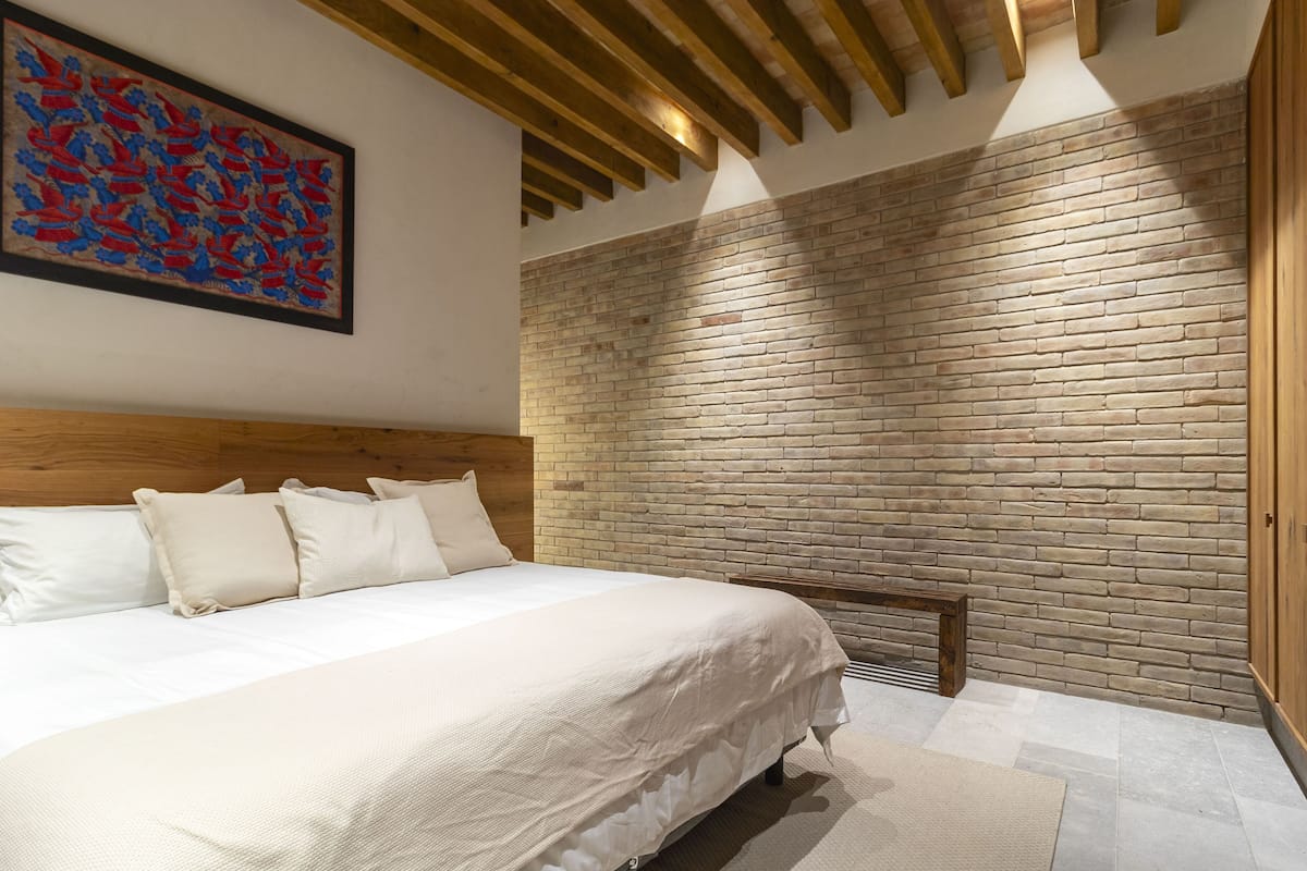 A bedroom with a large bed, a wooden headboard, a brick wall, and a wooden ceiling.