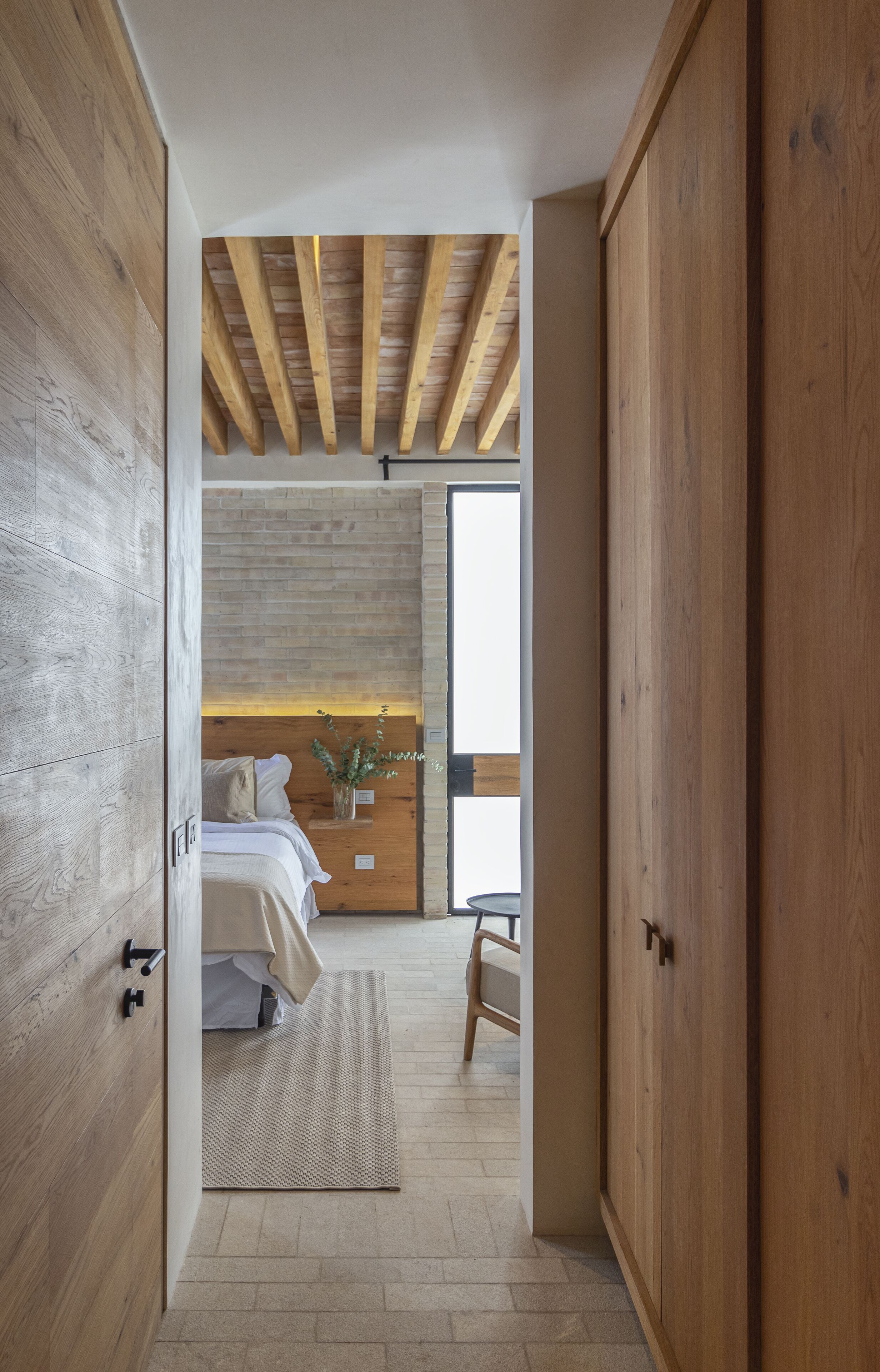 A bedroom with a bed, a nightstand, a potted plant, and a window.