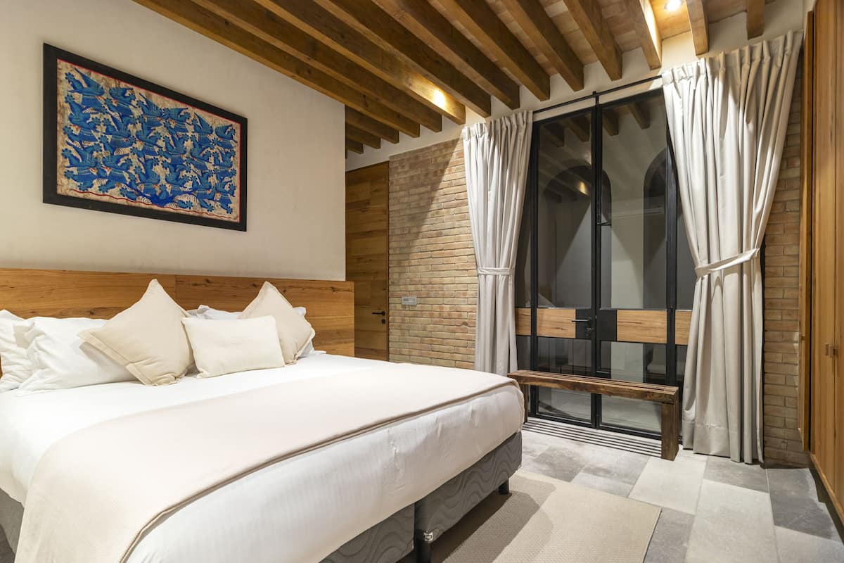 A bedroom with a large bed, wooden headboard, and a view of a balcony with curtains.