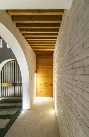 Un pasillo con techo de madera, paredes de ladrillo blanco y una puerta de metal.