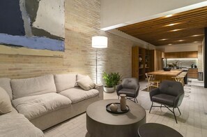 Una sala moderna con un sofá, dos sillones, una mesa de centro y un comedor con una mesa y sillas de madera.