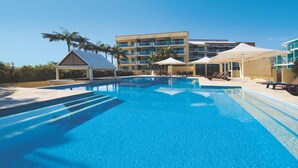 Una piscina con sillones de descanso y sombrillas, rodeada por un edificio con varios balcones.