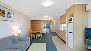 A compact living space with a sofa, dining table, chairs, a kitchenette, and a television. - The Entrance Waterfont Apartment 303 (The Entrance)