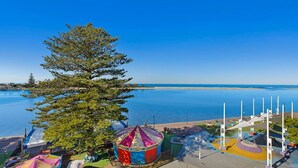 A coastal view with a large tree, a colorful tent, and a clear blue sky. - The Entrance Waterfont Apartment 303 (The Entrance)