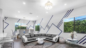 Un salon moderne avec un canapé d’angle, une table basse en verre et un coin repas comprenant une table et des chaises blanches.