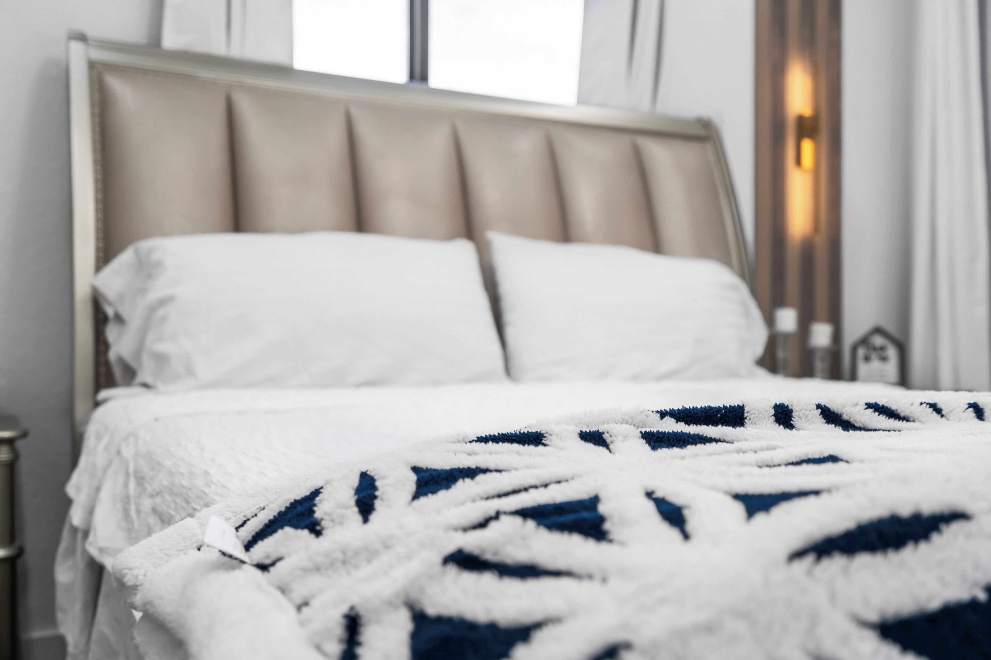 A bed with a white and blue patterned blanket, a headboard, and a bedside table with a lamp.