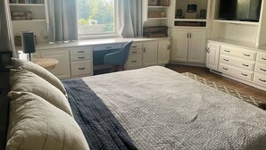 A bedroom with a bed, a desk, a chair, a bookshelf, a TV, and a ceiling fan.