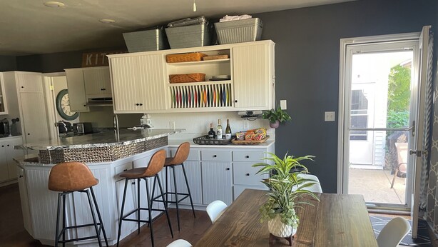 A modern kitchen with white cabinetry, a wooden island with bar stools, and a dining table with chairs.