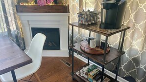 A cozy living room with a fireplace, a coffee machine, and a bookshelf.