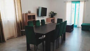 Ein Konferenzraum mit großem Tisch, grünen Stühlen, einem Flachbildfernseher und einem Blumentopf.