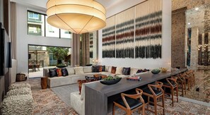 A modern dining area with a long table, multiple chairs, and a large hanging light fixture.