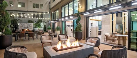 A spacious outdoor patio with a central fire feature, surrounded by wicker furniture and potted plants.