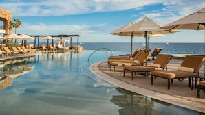 Un área de piscina con sillones de descanso y sombrillas, cielo despejado y vista al mar.