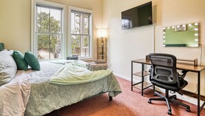 Une chambre à coucher avec un lit, un bureau avec une chaise, une télévision et un miroir avec des lumières.