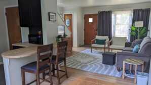 A living room with a sofa, chairs, a coffee table, and a kitchen area with a microwave and cabinets.
