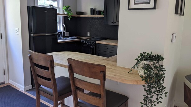 A modern kitchen with a wooden island, two chairs, a refrigerator, a stove, and a sink.