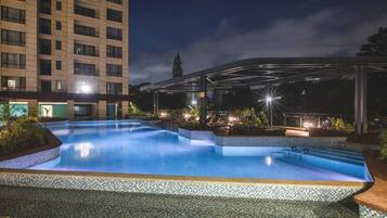 A swimming pool with a tiled edge, surrounded by a covered area with seating and lighting.
