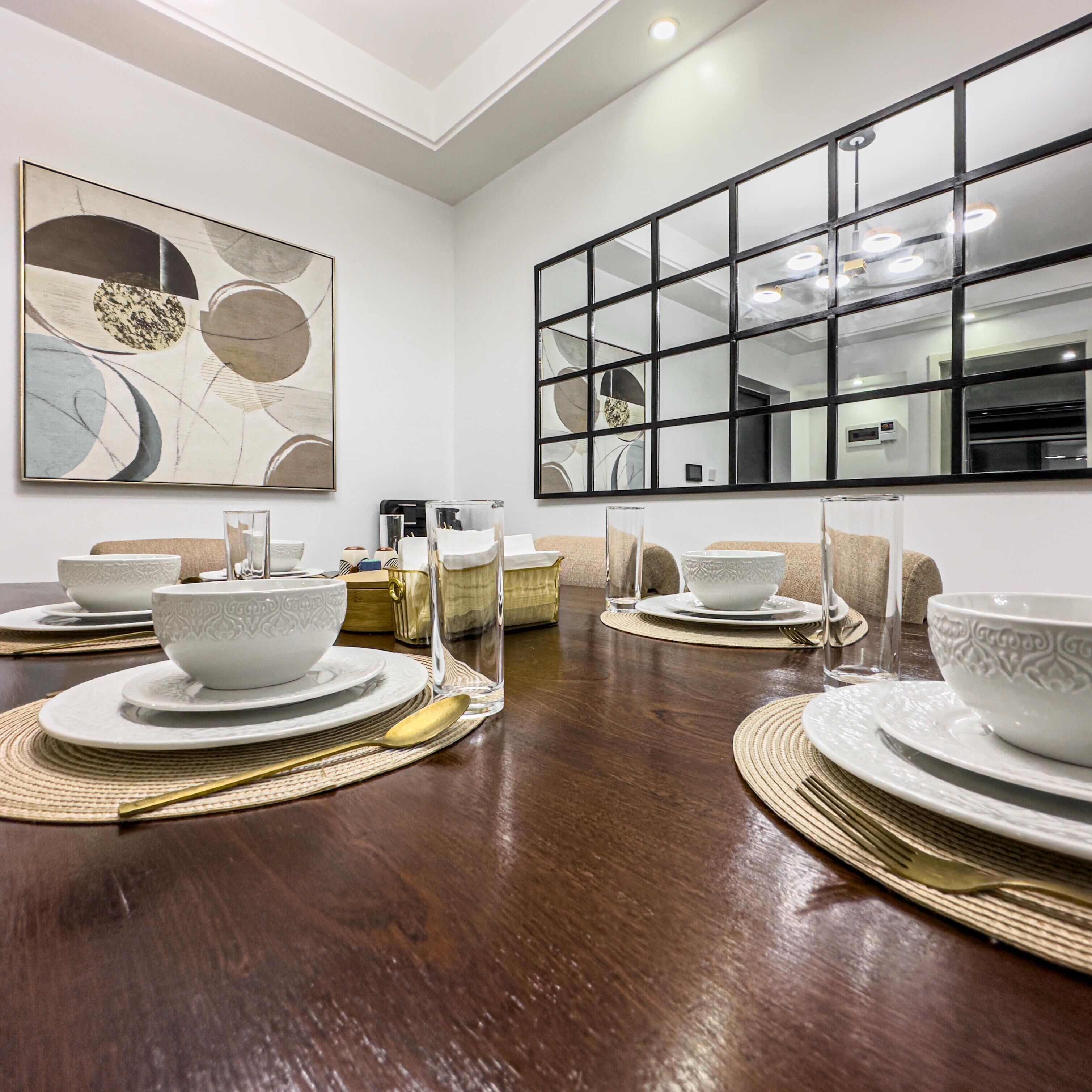 A dining area with a long wooden table set for a meal, featuring white plates, bowls, and cutlery.
