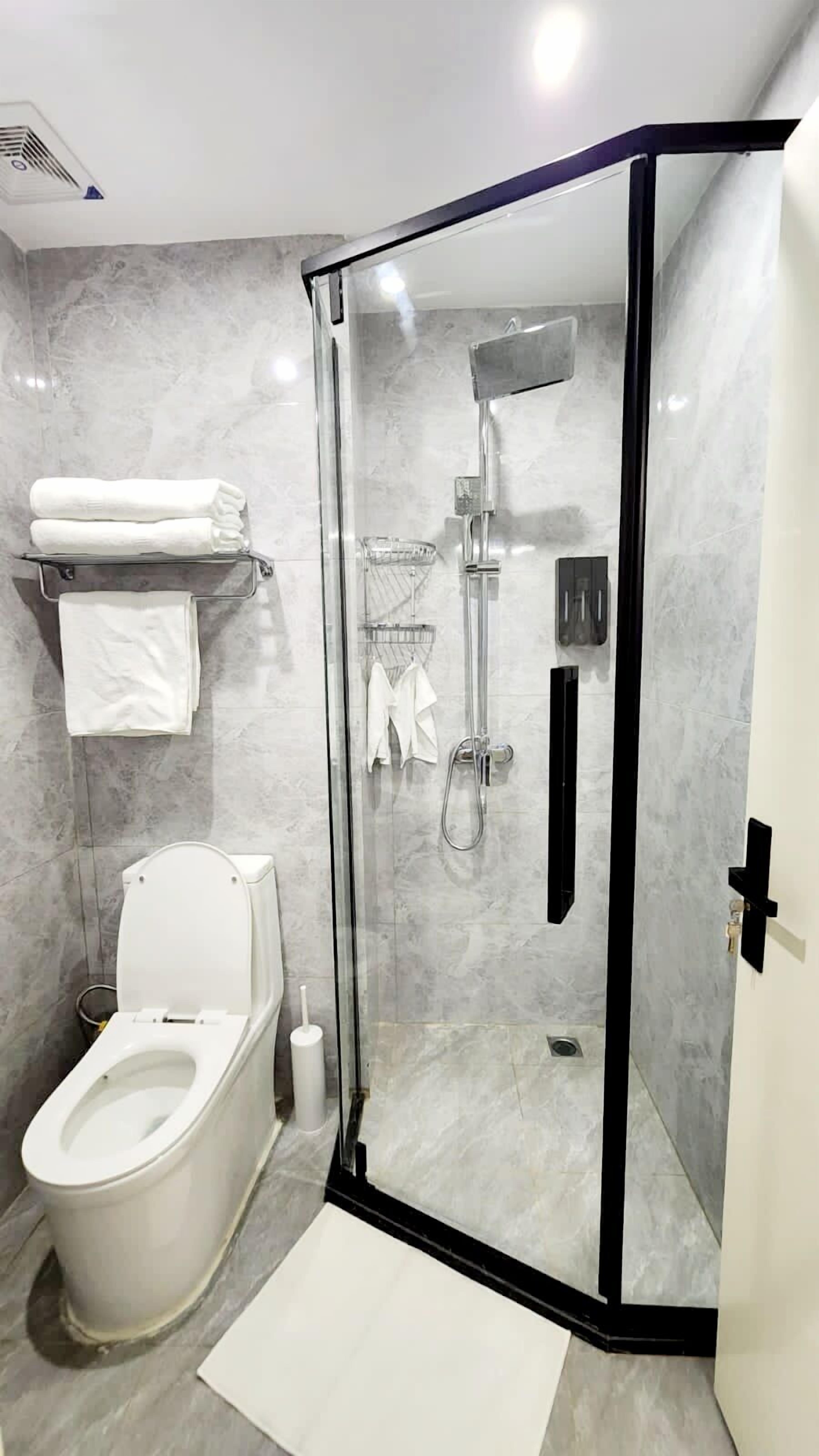 Une salle de bain moderne avec une douche à parois de verre, des toilettes et un porte-serviettes avec des serviettes pliées.