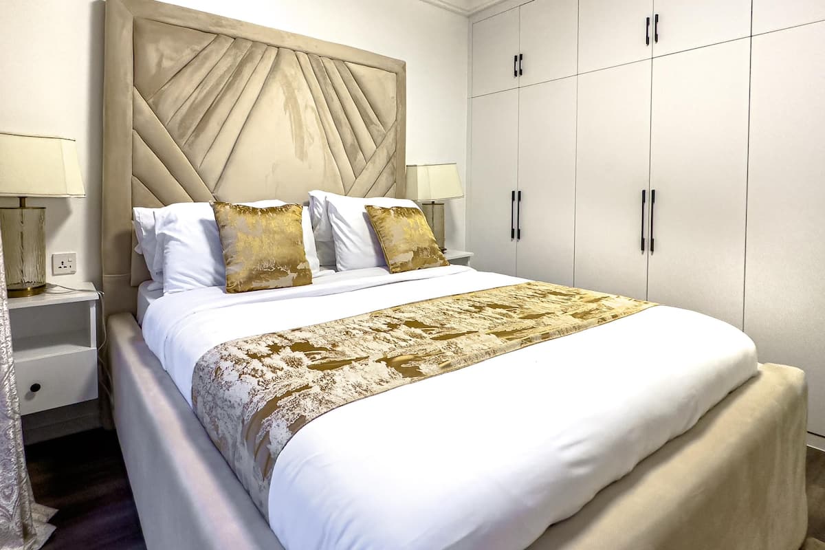 A neatly arranged bedroom with a large bed, a headboard, bedside tables, and a wardrobe.