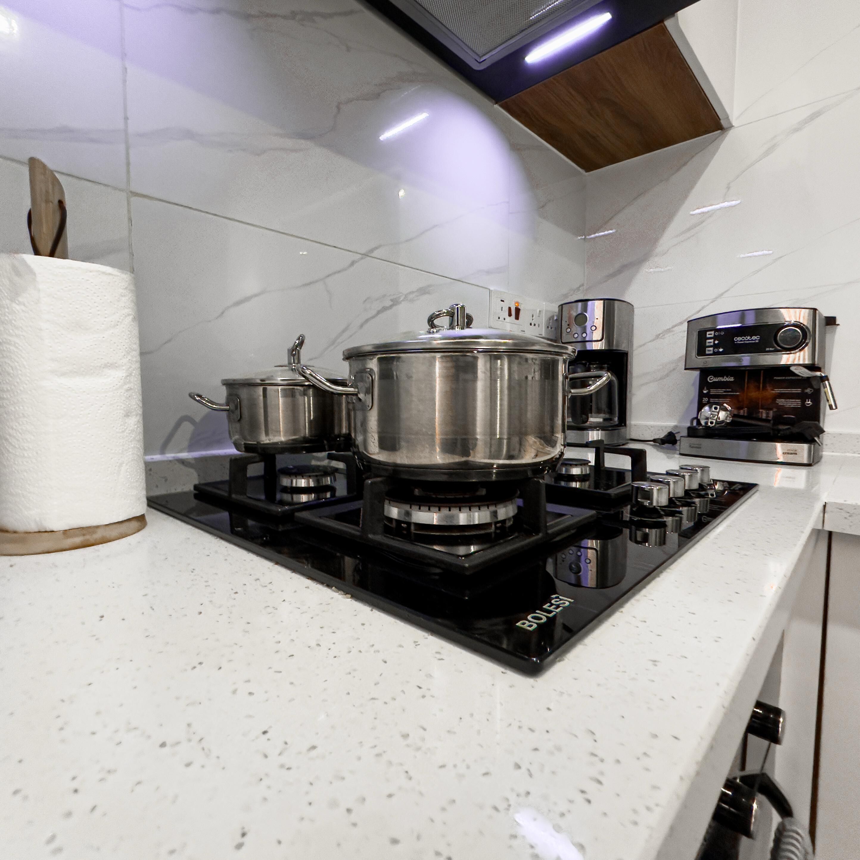 A kitchen with a black stove top, two pots, a coffee maker, and a roll of paper towels.