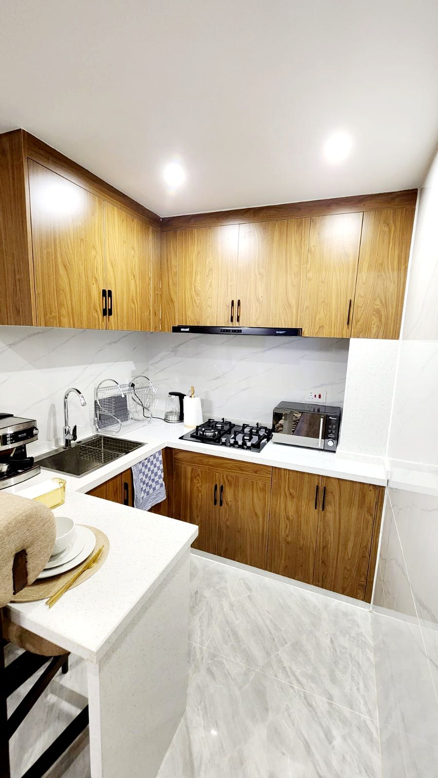 A modern kitchen with wooden cabinets, a white countertop, a gas stove, a microwave, and a sink.
