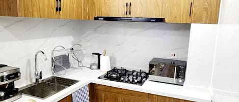 Eine moderne Küche mit Holdekor-Schränken, einer weißen Arbeitsplatte, einem Gasherd, einer Mikrowelle und einem Spülbecken.