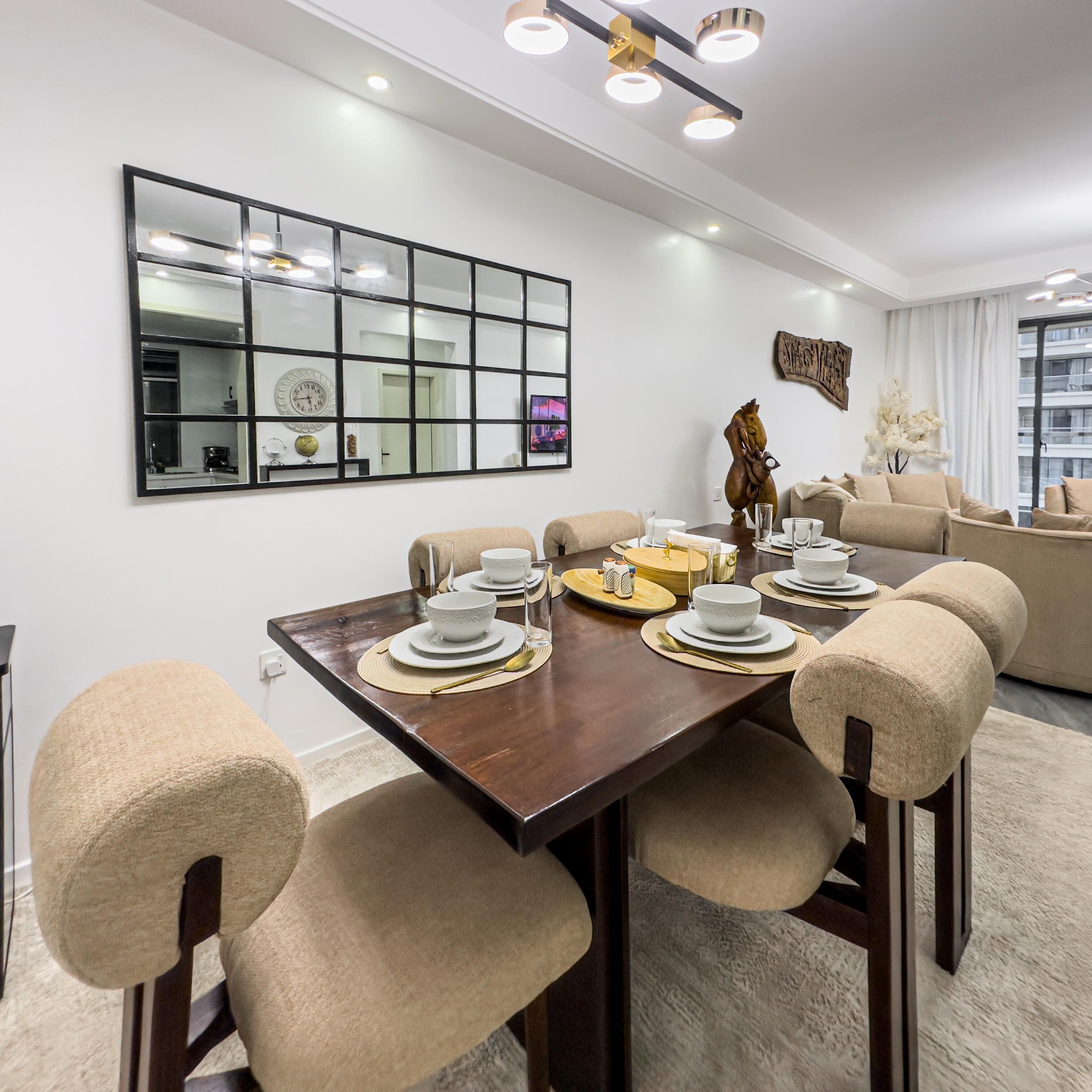Uma área de jantar com mesa de madeira posta para seis pessoas, rodeada por cadeiras bege.