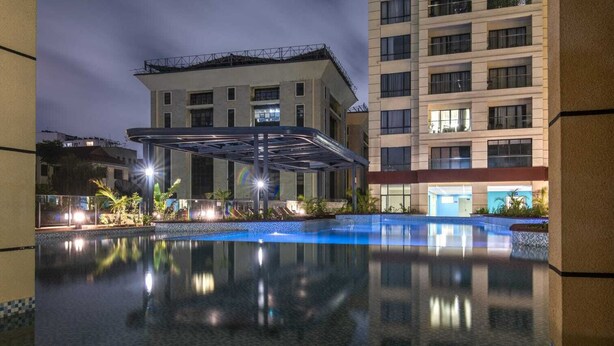 Un hotel moderno con piscina, un área exterior cubierta y un edificio de varios pisos al fondo.