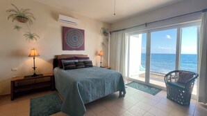 A bedroom with a bed, two bedside tables with lamps, a large window with a view of the sea, and a ceiling fan. - SEA CLIFF, 4-bedroom Economical, Oceanfront House, Isla Mujeres (Isla Mujeres)