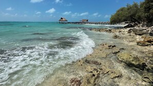 A beach with clear turquoise water, rocky shore, and overwater bungalows. - SEA CLIFF, 4-bedroom Economical, Oceanfront House, Isla Mujeres (Isla Mujeres)